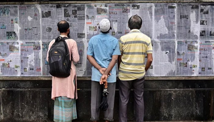Pedestrians read Bangladeshs local newspapers displayed along a street in Dhaka. — AFP