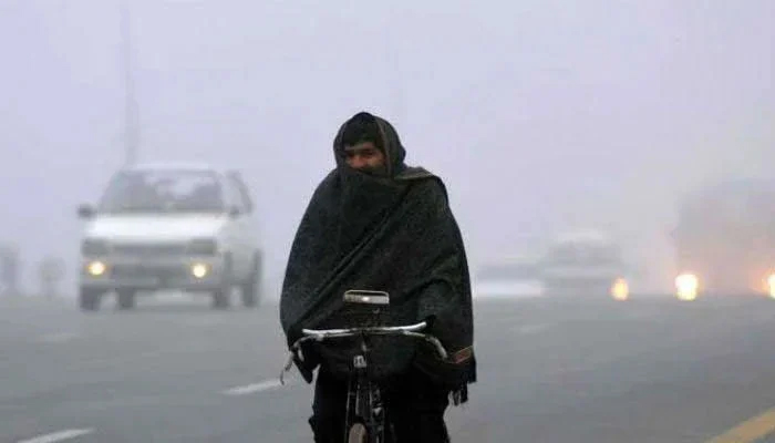 This representational image shows a man wrapped in shawl cycles on a road in Pakistan in cold weather. — AFP/File