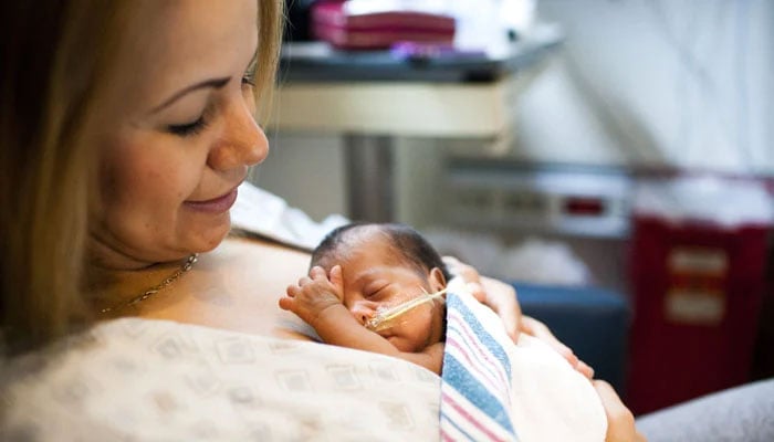 A premature baby lying in her mothers hands. — X/chc