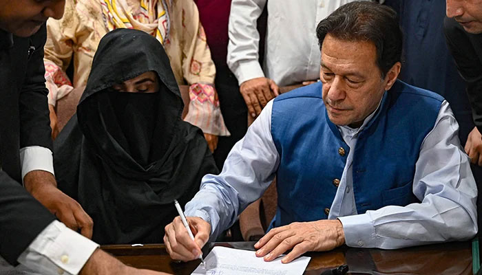 Former prime minister Imran Khan (right) along with his wife Bushra Bibi (centre) signs surety bonds for bail in various cases, at the registrars office in the Lahore High court on July 17, 2023. — AFP