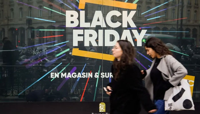 edestrians walk past a store window with a sign announcing Black Friday sales in Paris. — AFP File