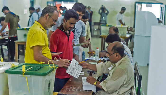 People stand in line up as election officials check their ballot papers during voting general election at a polling station in Lahore. — AFP/File