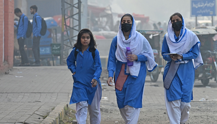 Students wearing face masks walk along a street amid smoggy conditions in Lahore on November 21, 2023. — AFP