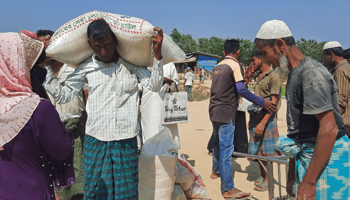 Rohingya refugees carry relief material after collecting from a distribution point in Kutupalong refugee camp in Ukhia on March 2, 2023. — AFP
