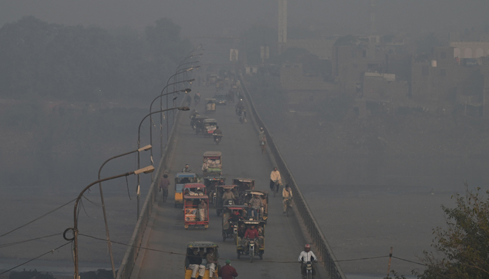 Commuters make their way along a street amid heavy smoggy conditions in Lahore on November 22, 2023. — AFP