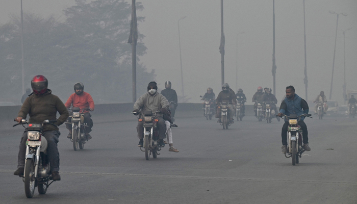 Commuters ride bikes along a street, amid heavy smog conditions in Lahore on November 24, 2023. — AFP