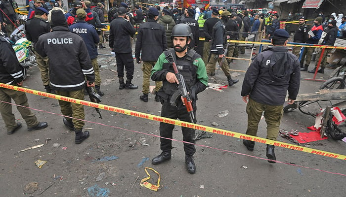 Lahore police official stands guard as others survey the crime scene. — AFP/File