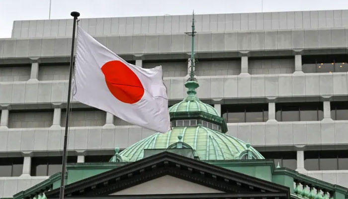 The Japanese flag flutters over the Bank of Japan (BoJ) head office building (bottom) in Tokyo on April 27, 2022. — AFP File