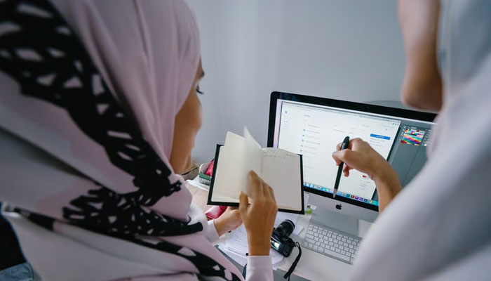 Representational image of two scarf-wearing women busy at their workplace. —Pexels