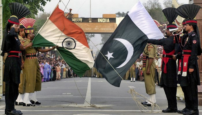 Pakistani (R) and Indian border security personnel hold flags of their country at the border. — AFP/File
