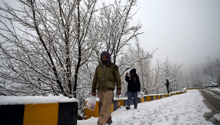 Residents walk during a snowfall in Murree. —AFP/File