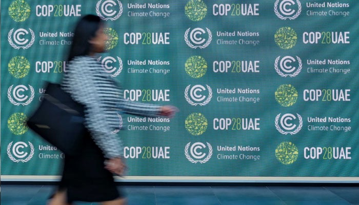 A woman walks by a wall that shows the logo of the 28th annual United Nations Climate Change Conference (COP28) being hosted by the United Arab Emirates (UAE) from November 30 to December 12, 2023. —AFP