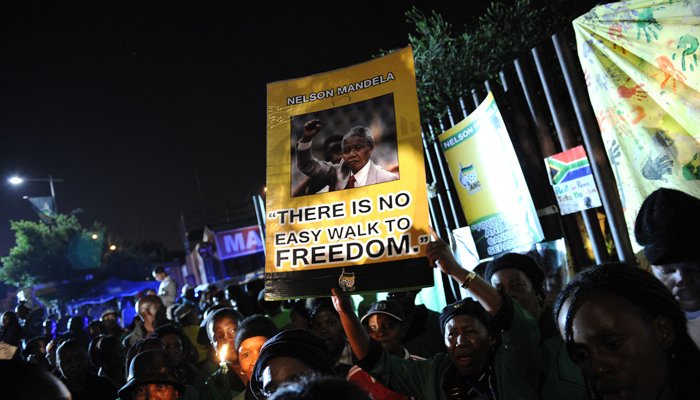 People sing to pay tribute to late former South African president Nelson Mandela outside his former house in Soweto. — AFP/File