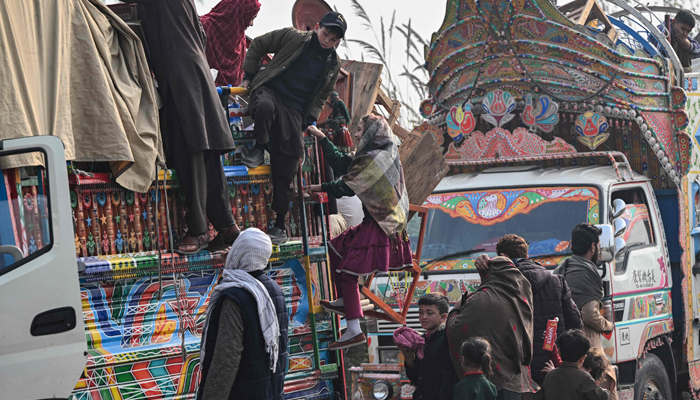 This photo taken on November 23, 2023 shows Afghan refugees climbing on a truck after visiting the UNHCR Azakhel Voluntary Repatriation Centre in Nowshera. — AFP