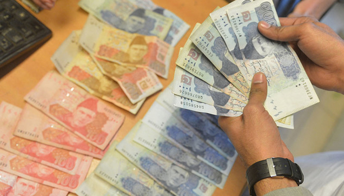 A money changer counts Rupee notes at a market in Karachi. — AFP/File