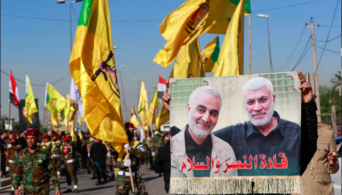A man lifts a placard depicting slain Iranian commander Qasem Soleimani (L) and Iraqi commander Abu Mahdi al-Muhandis, as fighters bearing flags of Iraq and paramilitary groups, including al-Nujaba and Kataib Hezbollah, march during a funeral in Baghdad for five militants killed a day earlier in a US strike in northern Iraq, on December 4, 2023. — AFP