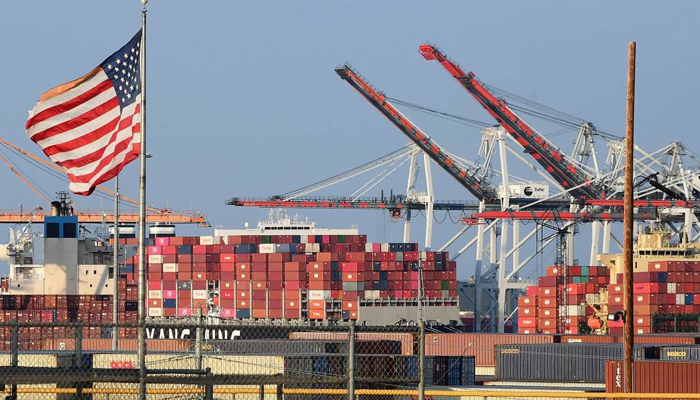 A US flag flies near containers stacked high on a cargo ship at the Port of Los Angeles, California. — AFP/File