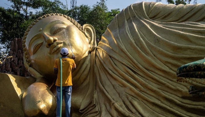 A worker cleans a Buddha statue at Maha Vihara Mojopahit temple in Mojokerto, ahead of the Vesak festival on May 31, 2023.—AFP