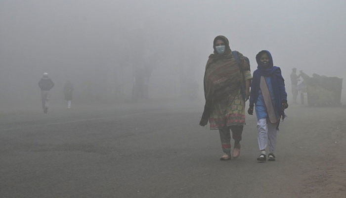 A student walks with her mother to school amid foggy weather in Lahore, Pakistan on December 21, 2022. — AFP