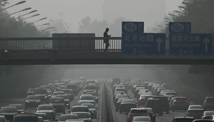 Pedestrians walk on an overpass as traffic snarls amid haze from air pollution in Beijing on November 1, 2023. — AFP File