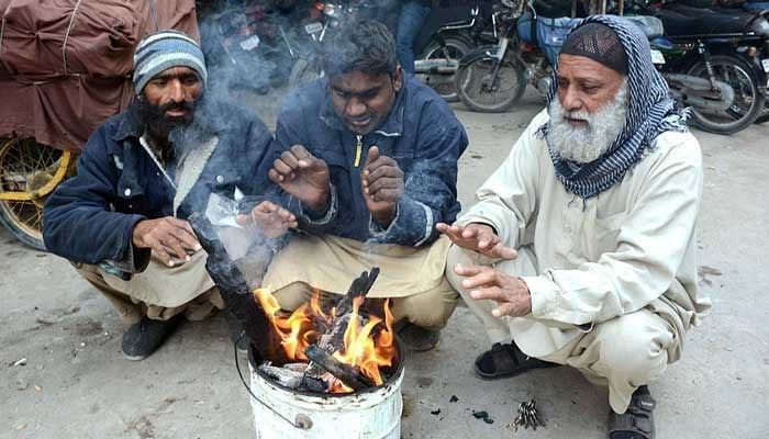 People sitting around wooden fire to keep them warm during chilled weather in city. — APP/File