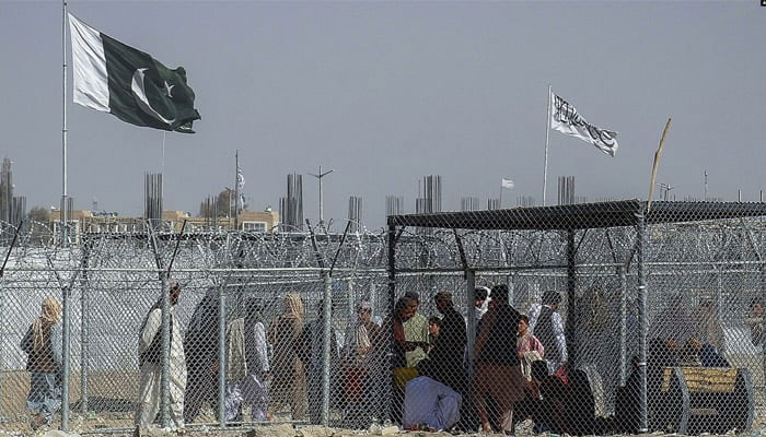 Afghan and Pakistani nationals walk through a security barrier to cross the border as the Pakistani and Taliban flags fly at the Pak-Afghan border crossing point in Chaman. — AFP/File