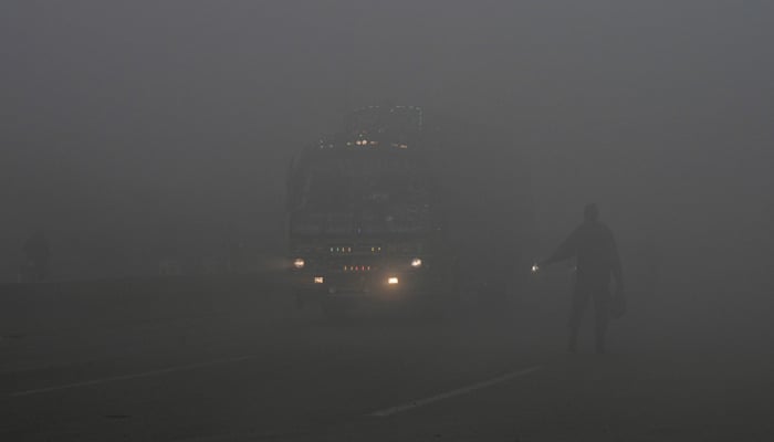 Commuters make their way along a street amid heavy smog in Lahore on December 14, 2023. — AFP