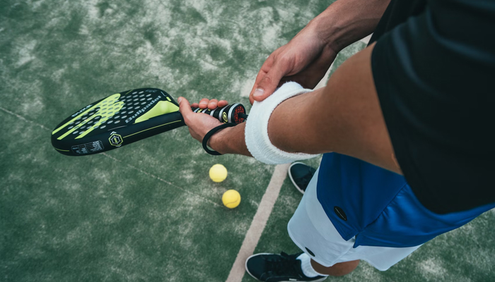 This representational image shows a person tightening the band on their arm while holding a racket. — Unsplash/File