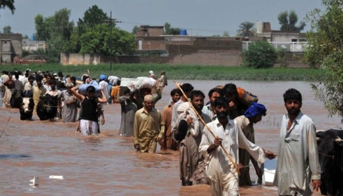 This picture shows people evacuating through floodwaters in the Mohib Bhanda area in Nowshera district. — AFP