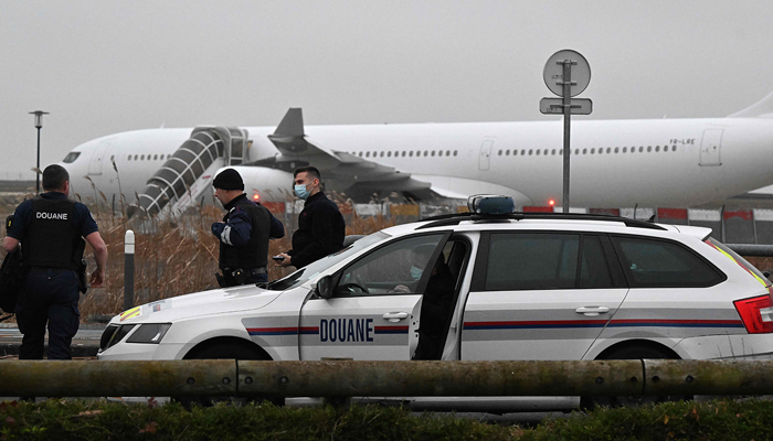 French customs officers stand next to a customs car with an Airbus A340 in the background which was grounded on the tarmac since December 21 over suspected human trafficking, at the Vatry airport, north-eastern France on December 25, 2023. — AFP