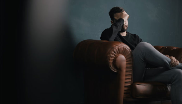 Representational image of a stressed man sitting in a dark room. — Unsplash