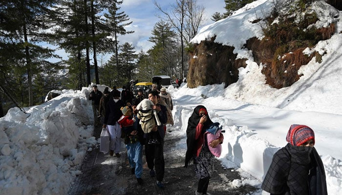 Tourists walk along a snow-covered road in Murree, Islamabad on January 9, 2022. — AFP