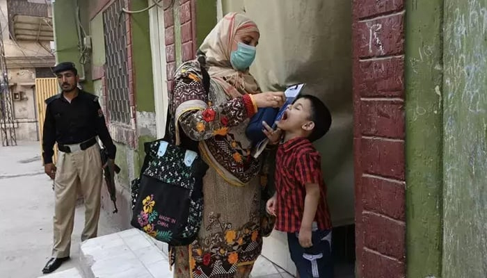 A health worker, escorted by a police officer, administers polio vaccine drops to a child during a vaccination campaign in Peshawar. — AFP/File