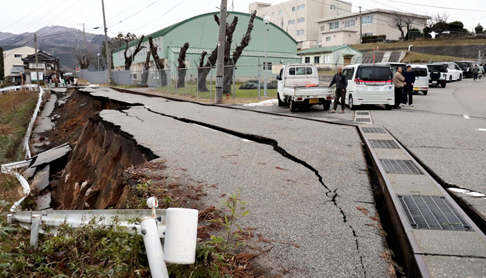 People stand next to large cracks in the pavement after evacuating into a street in the city of Wajima, Ishikawa prefecture on January 1, 2024. — AFP