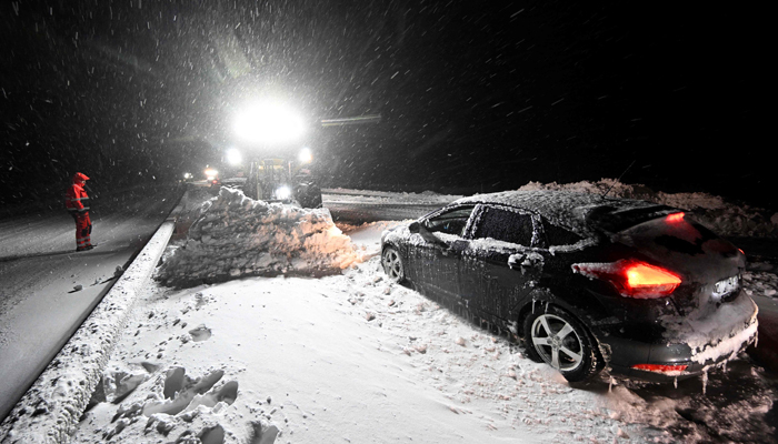 Employees cleared snow with wheel loaders as drivers are evacuated with the Home Guards tracked vehicle at Ekerodsrasten on the E22 between Horby and Kristianstad in southern Sweden, on the night of January 4, 2024. — AFP