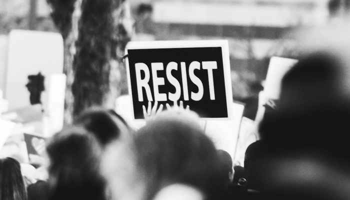 This representational image shows a person holding a placard of resist. — Pexels