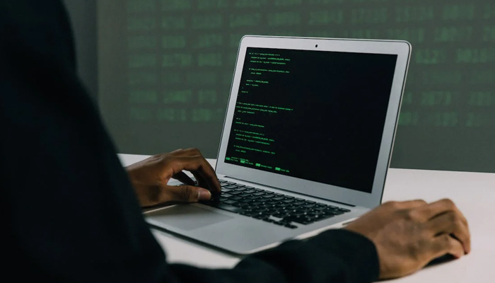 This image shows a person using a laptop showing coding. — Pexels
