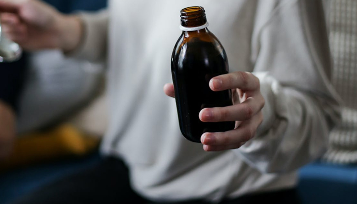 A representational image of a person holding a bottle of syrup. — Pexels