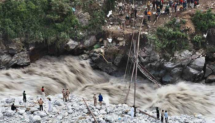 Men stand on the banks of a water stream caused by flooding in Chitral. — AFP/File