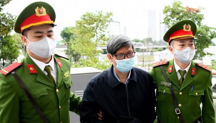 Vietnams former minister of health Nguyen Thanh Long (C) is led into a court by police for his anti-corruption trial over Covid test kit production bribes in Hanoi on January 3, 2024. — AFP