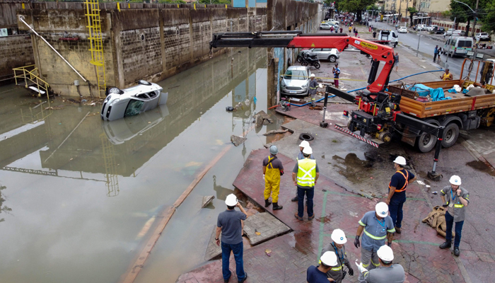 People look at a car which was swept into the flooded railways of the Acari metro station after heavy rains caused destruction in the suburbs of Rio de Janeiro, Brazil, on January 14, 2024. — AFP