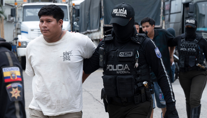 An agent of the Ecuadorian National Police escorts one of the several alleged members of the criminal gang Los Lobos captured during a police operation after they attacked a police post in Guayaquil, Ecuador on January 14, 2024. — AFP