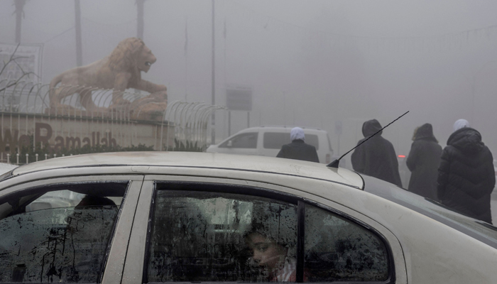 A child looks from inside a car as commuters walk past the landmark lion statue in early morning fog in the centre of the West Bank city of Ramallah on January 12, 2024. — AFP