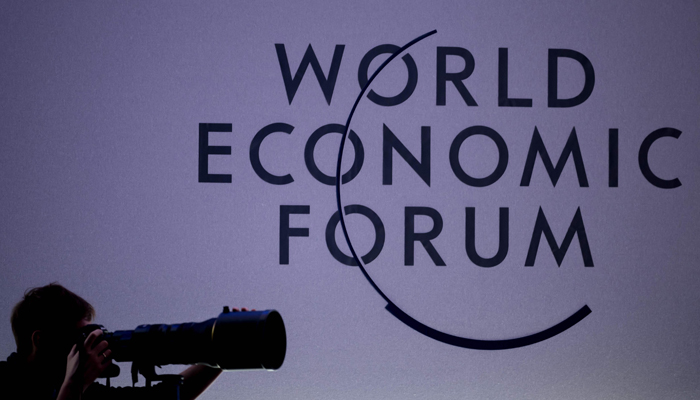 A press photographer works next to the logo of the World Economic Forum (WEF) at the opening of their annual meeting in Davos on January 15, 2024. — AFP