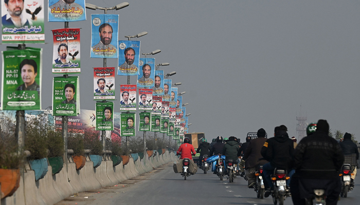 Commuters move past the election campaign posters ahead of the upcoming general elections in Rawalpindi on January 9, 2024. — AFP