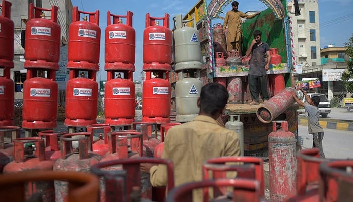 Labourers unload gas cylinders from a truck at a market on the outskirts of Islamabad. — AFP/File