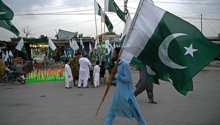 A man carrying Pakistans national flags walks through a street on the eve of the Independence Day celebrations in Peshawar on August 13, 2023. — AFP