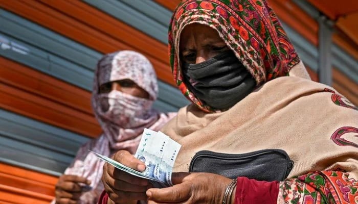 A woman in a face mask counts rupee notes as she walks on a street in Islamabad on April 9, 2020. — AFP