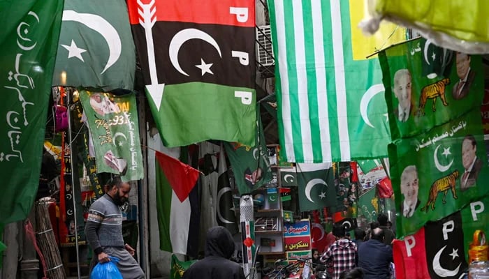 People walk past flags of Pakistans political parties displayed for sale at a market in Lahore on January 13, 2024, ahead of the country´s general elections. — AFP
