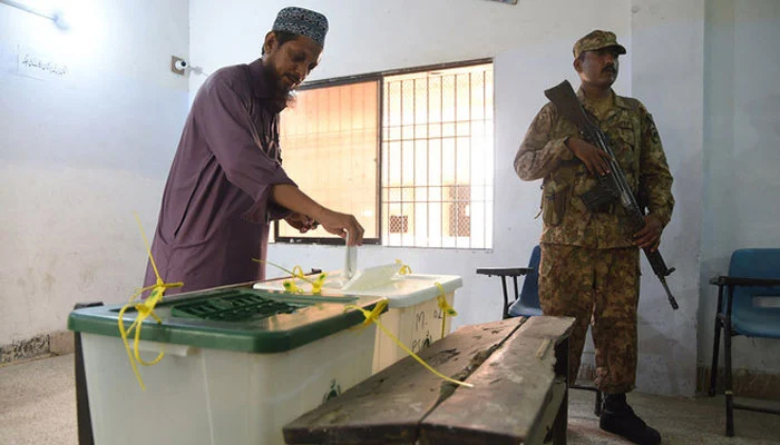 A man casts his vote as a soldier stands guard at a polling station during the general election in Karachi on July 25, 2018. — AFP